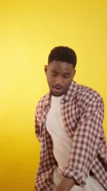 Enerjik genç adam dinamik pozlar ve parlak sarı stüdyo arkaplanına karşı anlamlı jestler sergiliyor, çağdaş tarzı ve kendinden emin vücut dilini sergiliyor.