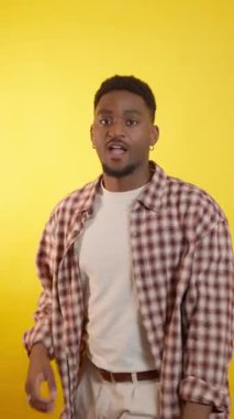 Genç erkek, dinamik bir şekilde el hareketleriyle ve vücut hareketleriyle canlı sarı stüdyo arkaplanına karşı iletişim kuruyor.