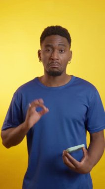 Mavi gömlekli genç profesyonel elinde yeşil ekranlı akıllı telefon, canlı sarı stüdyo arka planına karşı duruyor.