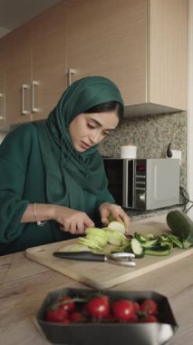Ön planda vişneli domateslerle ahşap bir tahtanın üzerinde salatalık doğrayan bir kadının yavaş çekim videosu.