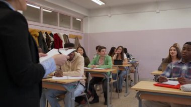 Bir derse katılan özenli öğrencilerle sınıf tartışmasına liderlik eden öğretmen. Çeşitli gruplar öğrenme ortamı içindeler