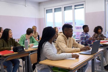 Çeşitli lise öğrencileri parlak bir sınıfta derse katılıyor, öğreniyor ve işbirliği yapıyorlar.