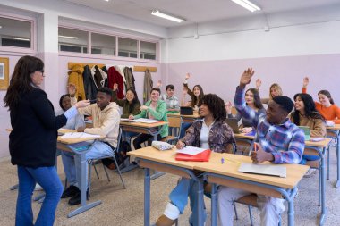 Çok ırklı öğrenciler, öğretmenin sorusuna cevap vermek için coşkuyla el kaldırarak, aktif öğrenmeyi teşvik ediyorlar.