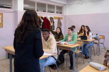 Çok ırklı öğrenciler, lise enstitüsünde ders sırasında öğretmenlerin sorularını yanıtlamak için ellerini kaldırıyorlar.