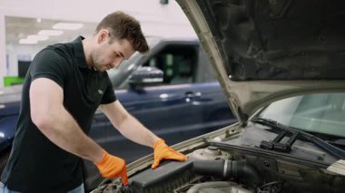 Profesyonel araç bakım servisi sırasında detaylı motor denetimi yapan turuncu eldivenli deneyimli otomotiv teknisyeni.