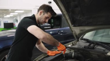Profesyonel araba servis merkezi çevresindeki araç motoru üzerinde detaylı teşhis ve onarım çalışmaları yapan yetenekli bir otomotiv teknisyeni.