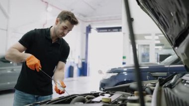 Araba tamirhanesinde araba bakım sırasında motor yağı seviyesini dikkatlice inceleyen profesyonel bir tamirci.