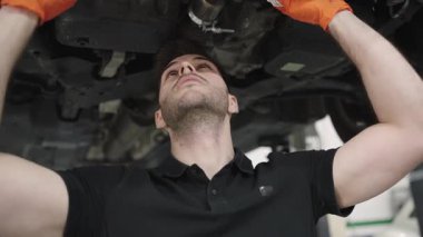 Profesyonel tamirci koruyucu turuncu eldivenler giyiyor. Tamir atölyesinde detaylı otomotiv servisi sırasında arabanın bagajını dikkatle inceliyor.