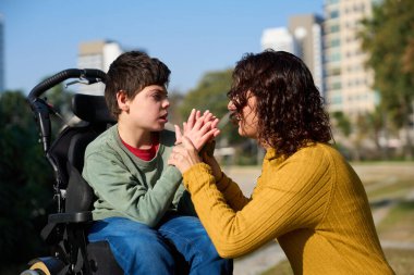 Mutlu bir anne oğluyla meşgul, neşeli anlar paylaşıyor. Parkta güneşli bir günün tadını çıkarıyor. Doğayla iç içe.