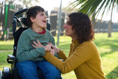 Mutlu çocuk, annesiyle birlikte parkta gülüyor ve güneşli bir günün tadını çıkarıyor.