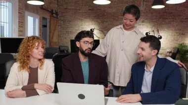 Takım üyeleri, stratejik proje planlaması sırasında çağdaş iş yerinde gülümserken laptopta yenilikçi fikirleri paylaşarak sıcak bir işbirliği içinde çalışırlar.