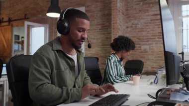 Kulaklık ve klavye kullanan bir ofis çalışanı, ortak çalışma alanında müşteri desteği veya çevrimiçi hizmetler sunuyor. Yavaş çekim