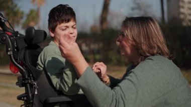 Anne engelli oğluna yardım ediyor ve onunla etkileşime geçiyor. Park ortamında bakım ve destek sağlıyor.