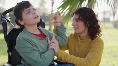 Şefkatli bir anne, barışçıl park gezintisi sırasında tekerlekli sandalyedeki engelli oğluyla şefkatli bir destek ve duygusal bir bağ sağlıyor. Ailevi sevgi ve anlayış gösteriyor.