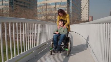 Sevgi dolu anne engelli oğluyla tekerlekli sandalyeyi şehir köprüsünden iterek güçlü bir aile bağı ve destekleyici bir ilişki gösteriyor.