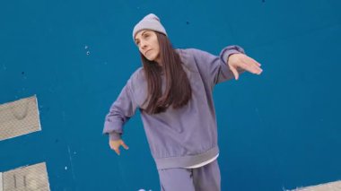 Hip hop dansçısı canlı mavi duvara karşı dinamik, anlamlı hareketler sergiliyor, sokak dansı stili, enerji ve tutku ve yaratıcılıkla sanatsal hareketler sergiliyor.