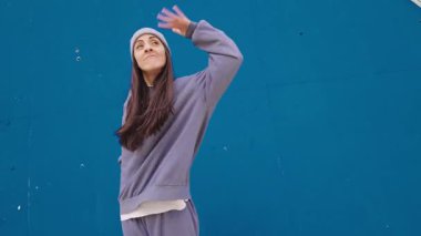 Hip hop dansçısı canlı mavi duvara karşı dinamik hareketler sergiliyor, tutkulu sanatsal hareketler ve çağdaş sokak dansı tarzıyla enerjisini ifade ediyor.