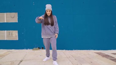 Dişi hip hop dansçısı mavi şehir duvarının yanında dinamik koreografi sergiliyor, tutkulu sokak dansı stili ile sanatsal hareketleri ifade ediyor.