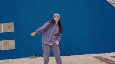 Genç bayan dansçı canlı mavi duvara karşı dinamik hip hop hareketleri sergiliyor, çağdaş şehir dans tarzı ve hareketlerini vurguluyor.