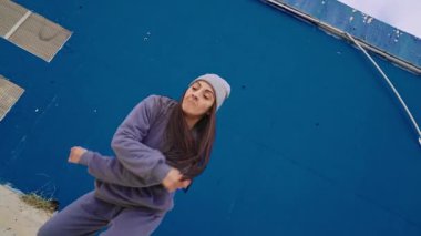 Dinamik hip hop koreografisi yapan kadın dansçı enerjik şehir tarzı ve çağdaş ritimle canlı mavi arka plana karşı tutkulu bir hareket sergiliyor.