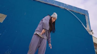 Dinamik hip hop koreografisi yapan kadın dansçı, güçlü, ritmik tarzda canlı mavi arka plana karşı kentsel enerji ve sanatsal hareketi ifade ediyor.