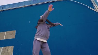 Enerjik bayan dansçı, canlı mavi bir duvara karşı hareketli, dinamik hareketler ve etkileyici bir stil sergileyen bir hip hop gösterisi sergiliyor.