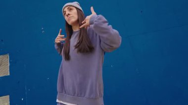 Enerjik bayan dansçı büyüleyici bir hip hop gösterisi sergiliyor canlı bir mavi arka plana karşı