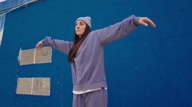 Genç bayan dansçı dinamik hip hop hareketleri yapıyor canlı mavi duvara karşı, enerjik koreografi ve şehir tarzı ile tutkuyu ifade ediyor.