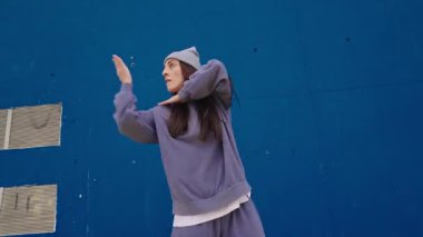 Hip hop dansçısı canlı mavi duvara karşı tutkulu enerjisiyle dinamik, anlamlı hareketler sergiliyor, kentsel dans stili ve çağdaş hareket becerileri sergiliyor.