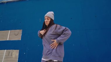 Hip hop dansçısı dinamik, enerjik hareketler sergiliyor canlı mavi duvara karşı etkileyici hareketler sergiliyor, kentsel dans kültürü ve sanatsal tutkuyu somutlaştırıyor.