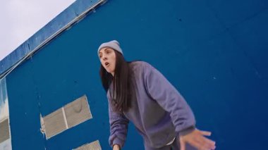 Kadın dansçı dinamik hip hop hareketleri yapıyor, şehir tarzı ve yaratıcı enerjisini canlı mavi duvar arka planına yansıtıyor, hareketli ve tutkulu
