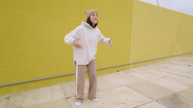 Ateşli kadın dansçı, dinamik hip hop gösterisi yapıyor, canlı sarı şehir duvarına karşı enerji ve yaratıcılık yayıyor.