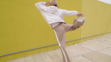 Dinamik hip hop hareketleri yapan kadın dansçı dışavurumcu enerjisiyle, canlı sarı arka plana karşı durarak sokak dansı kültürünü ve sanatsal hareketi temsil ediyor.