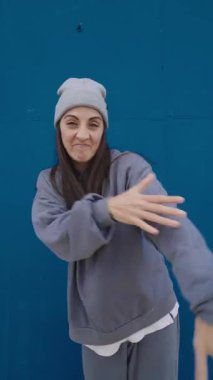 Enerjik hip hop dansçısı dinamik hareketler sergiliyor ve canlı mavi bir arkaplan karşısında ifadeler sergiliyor.