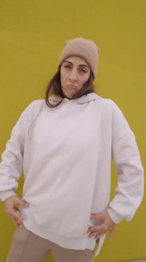 Enerjik bir kadın hip hop dansı yapıyor, dinamik hareketler sergiliyor ve hareketli sarı bir arkaplana karşı neşeli ifadeler sergiliyor.