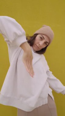 Parlak sarı duvara karşı dinamik hip hop koreografisi yapan kendinden emin kadın dansçı tutkulu hareketlerle enerji ve sokak dansı tarzını ifade ediyor.