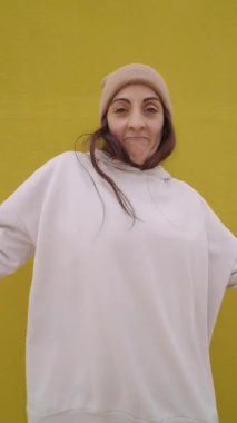 Genç bir kadın gündelik kıyafetler giyiyor ve parlak sarı bir arka planda hip hop dansı yapıyor.