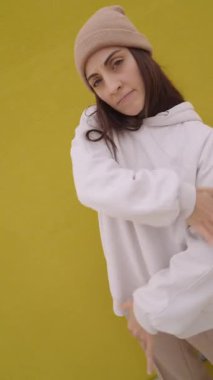 Hip hop dansçısı canlı sarı bir duvara karşı hareketler sergiliyor. Etkileyici jestler ve neşeli ifadeler sokak dansı sanatını ön plana çıkarıyor.