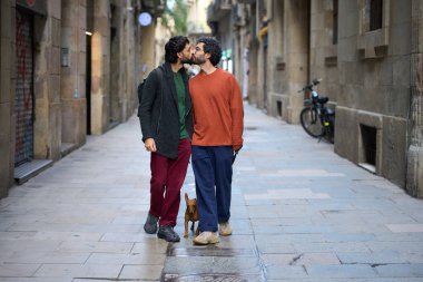 Barselona, İspanya 'da dar bir sokakta küçük kahverengi köpekleri ile yürürken birbirlerini öpen romantik eşcinsel çift.