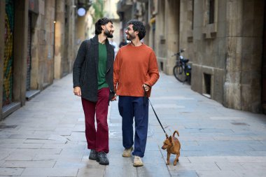 Neşeli bir Barselona caddesinde köpekleri ile el ele yürüyen mutlu eşcinsel çift, sevgi ve arkadaşlıkla dolu güneşli bir günün tadını çıkarıyor.