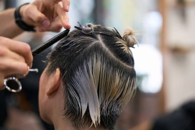 Saç ve makas kullanan kuaför, kuaförde kısa saçlı genç bir kadının ıslak saçlarını kesiyor.