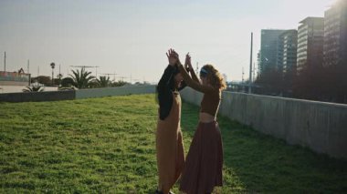 İki kadın, lgbt topluluğunun üyeleri, güneşli bir günde şehir parkında dans ediyorlar ve gülümsüyorlar.