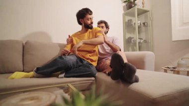 Mutlu eşcinsel çift, modern dairelerinde rahat bir kanepede rahatça sarılıp eğleniyor.