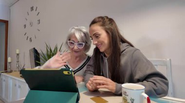 Büyük anne ve yetişkin kız video görüşmesi sırasında neşeli bir bağ paylaşıyorlar, dijital tabletle sıcak bir şekilde iletişim kuruyorlar.