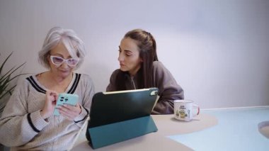 Evde akıllı telefon ve tablet kullanan büyük anne ve yetişkin kız kaliteli zaman ve dijital öğrenmenin keyfini çıkarıyorlar.