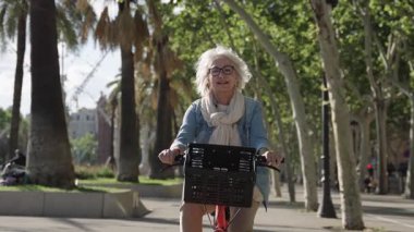 Güneşli bir parkta bisiklet sürmekten hoşlanan yaşlı bir kadın, yavaş çekim montajında görüntülendi.
