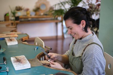 Bir mücevher atölyesinde elinde dosyayla çalışan gülümseyen bir zanaatkar. El yapımı mücevherler yapıyor.