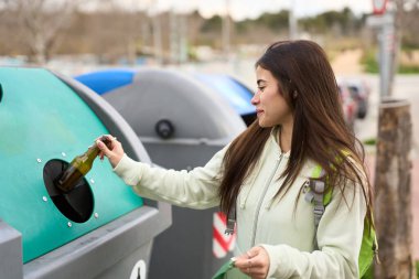 Sorumlu vatandaş, halka açık bir geri dönüşüm kutusunda cam bir şişeyi geri dönüştürerek çevresel sürdürülebilirliğe katkıda bulunuyor