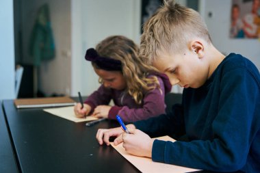 İki odaklanmış öğrenci ödevlerini özenle yapıyor, masadaki kağıtlara dikkatlice yazıyorlar.