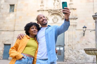 Mutlu çift Barselona, İspanya 'da, tarihi bir binanın önünde akıllı bir telefonla selfie çekiyor, tatillerinin tadını çıkarıyorlar.